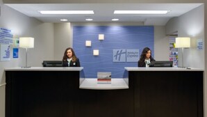 Un comptoir d’accueil avec deux employés, un mur bleu orné du logo et un petit livre posé sur le comptoir.