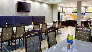 Un espace de restauration d’hôtel avec des banquettes et des tables, un téléviseur à écran plat fixé au mur, et un buffet en arrière-plan.