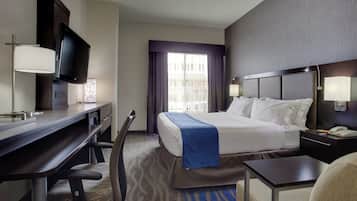 A hotel room with a bed, desk, chair, television, and a window with curtains.