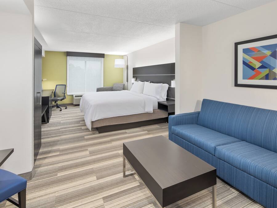 Una habitación de hotel con una cama, un sofá azul, una mesita pequeña y un escritorio con una silla.