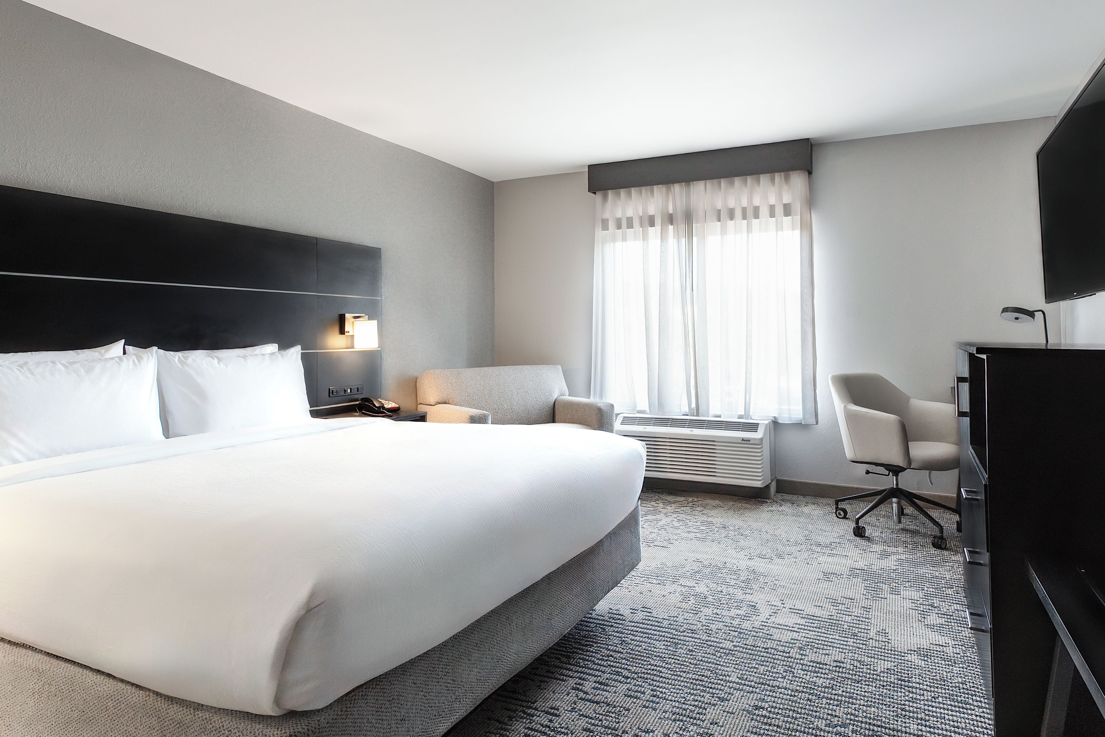 A hotel room with a large bed, a desk, a chair, and a television.