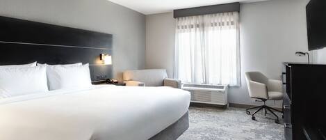 A hotel room with a large bed, a desk, a chair, and a television.