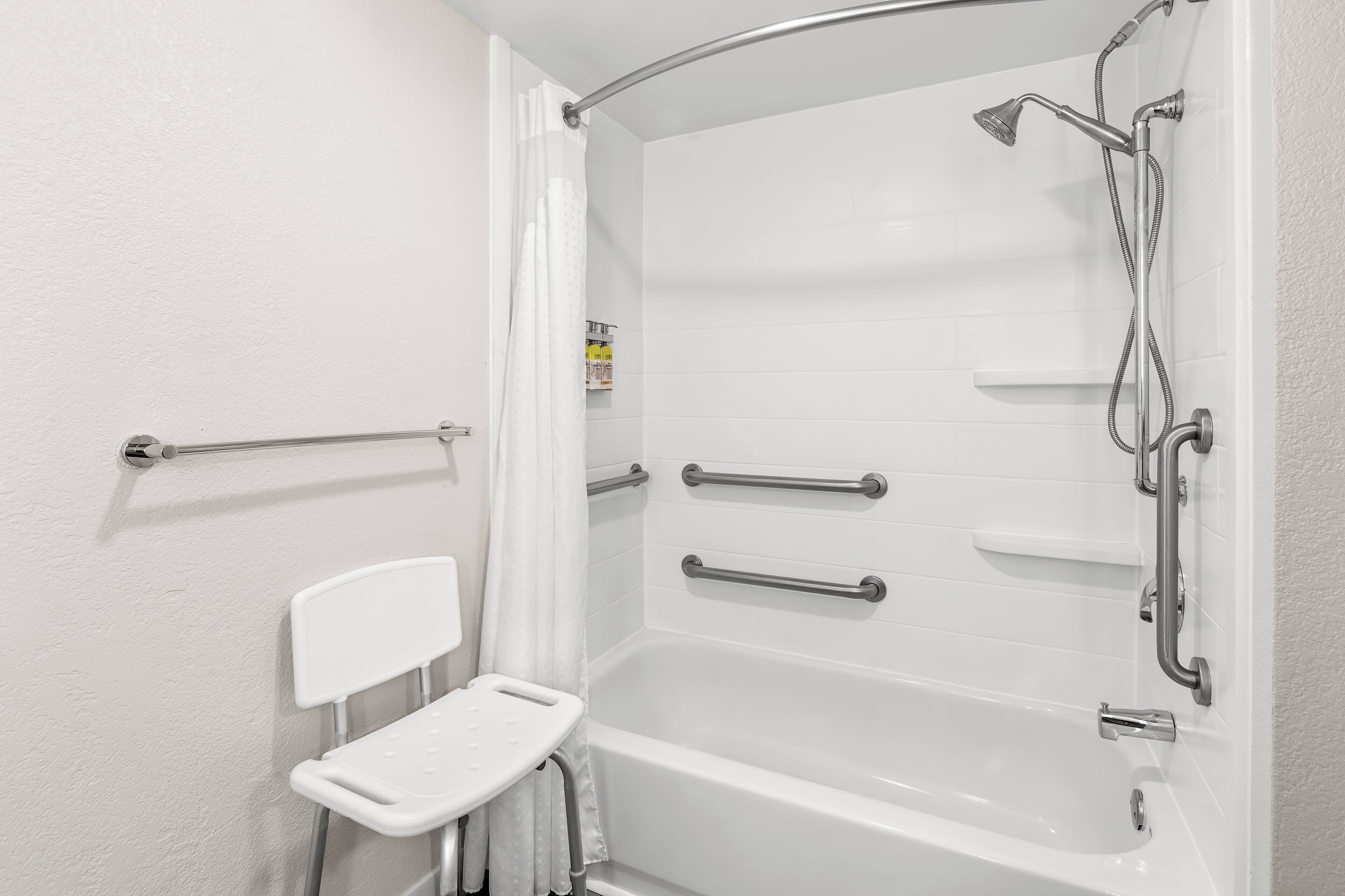 Une douche à l’italienne avec une barre d’appui, une baignoire blanche et un pommeau de douche.