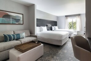 A hotel room with a bed, a sofa, a chair, a small table, and a painting on the wall.