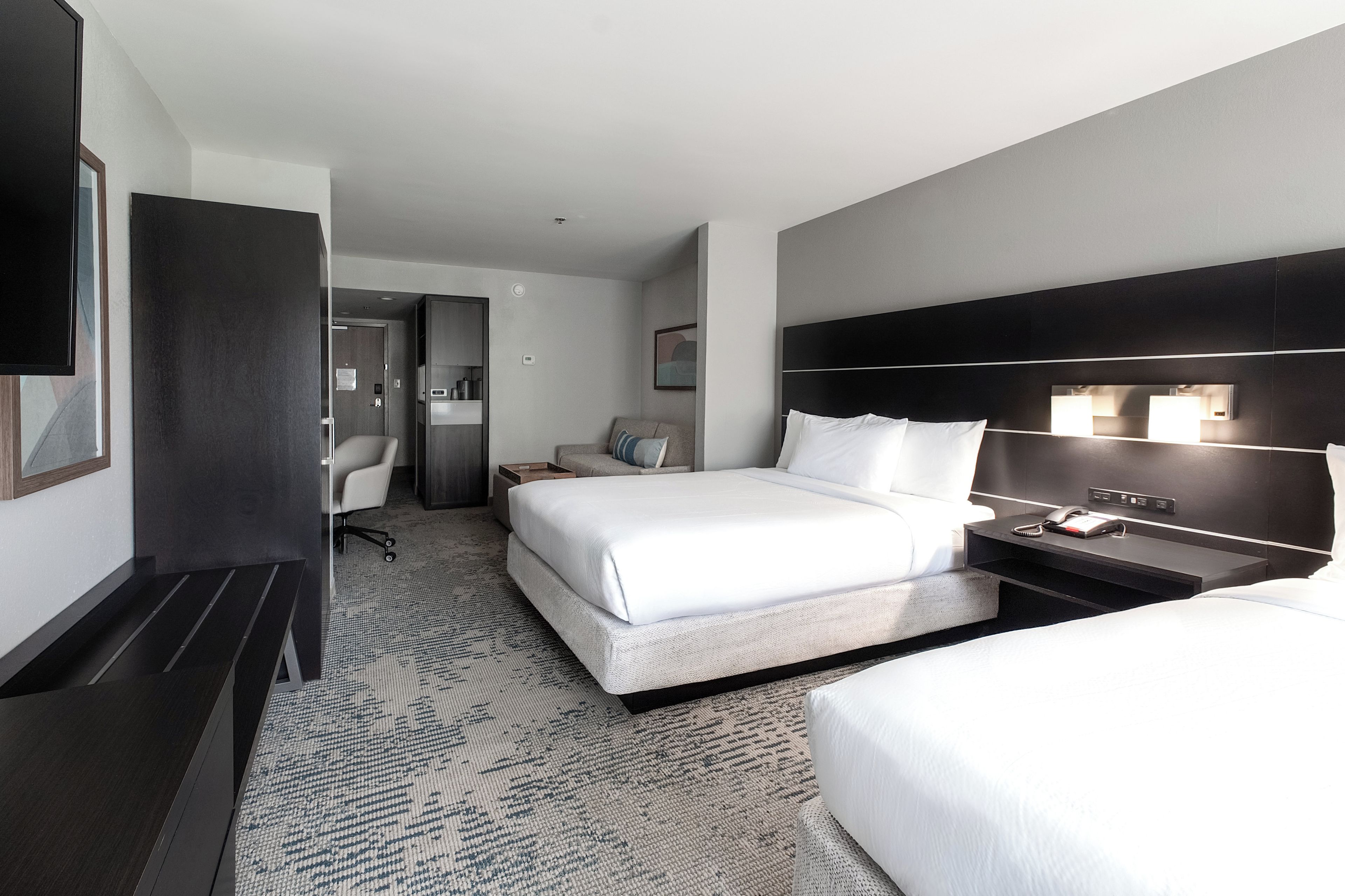A hotel room with a large bed, a bedside table with a lamp, a desk, and a chair.