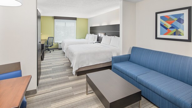 A hotel room with two beds, a blue sofa, a wooden coffee table, and a framed abstract painting on the wall. - Holiday Inn Express & Suites Greenville-I-85 & Woodruff Rd by IHG (Greenville)