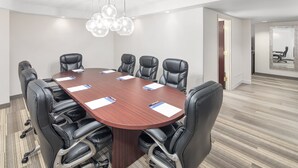A conference room with a large wooden table, black leather chairs, and a modern chandelier.