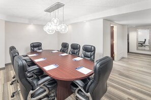 Une salle de conférence dotée d’une grande table en bois, de chaises en cuir noir et d’un lustre moderne.