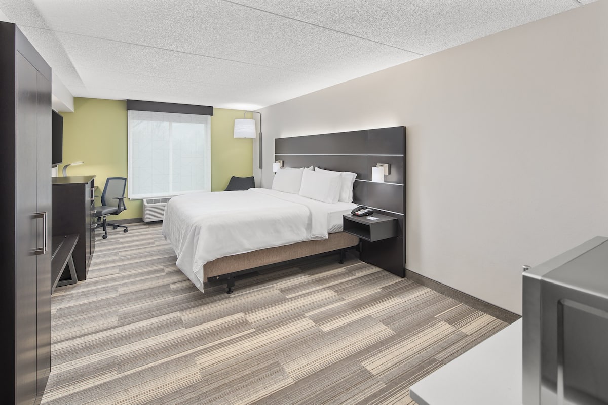 Une chambre d’hôtel moderne avec un lit bien fait, un bureau avec une chaise, une lampe de bureau et une table de chevet avec une lampe.