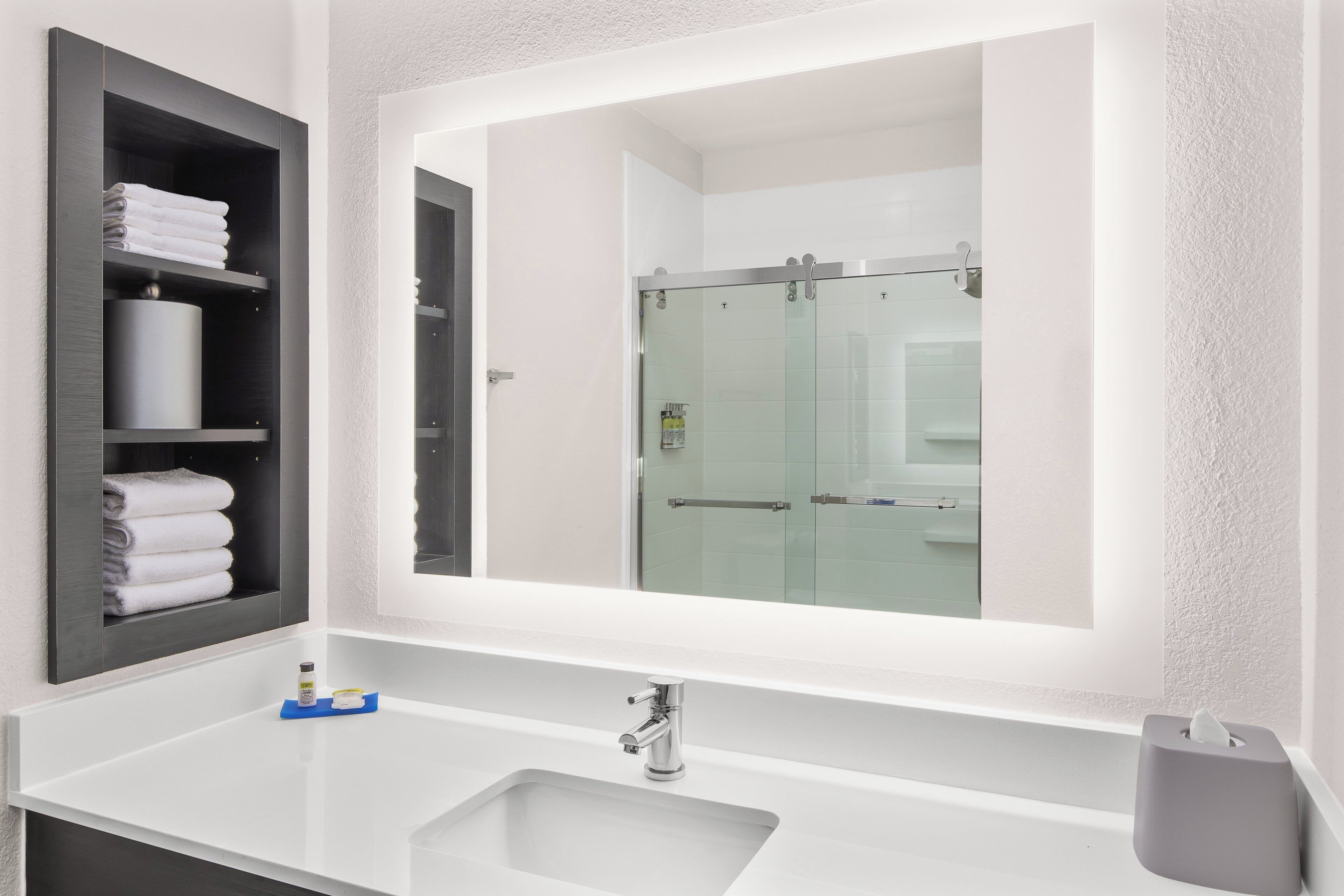 Een moderne badkamer met een grote spiegel, een witte wastafel en een douchecabine met glazen wanden.