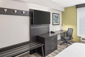 Een hotelkamer met een bed, een bureau met stoel, een flatscreen-tv en een bankje.