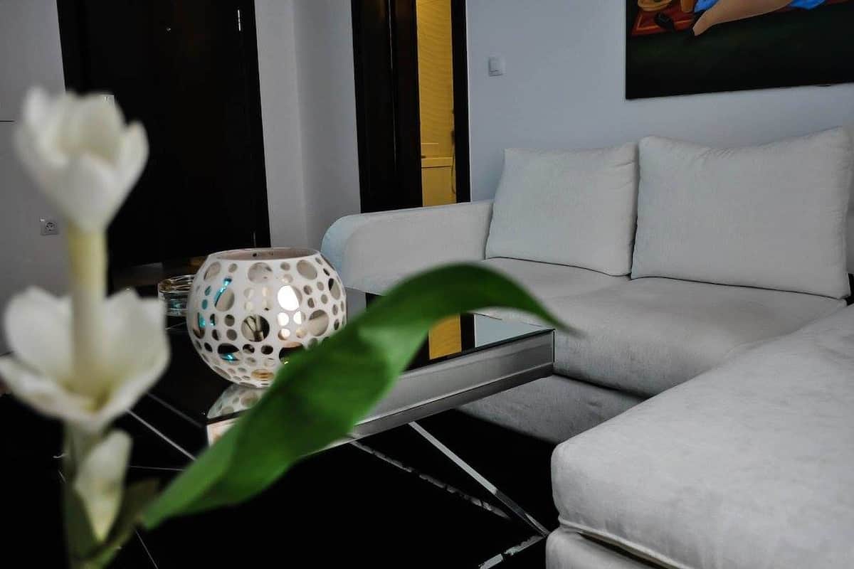 Un saló modern amb un sofà blanc, una taula de centre de vidre i un vas decoratiu blanc amb forats.