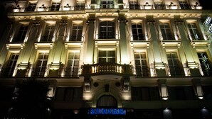 A grand hotel facade with illuminated windows and balconies, a prominent entrance with a decorative arch, and a sign reading "HOTEL". - Andromeda Hotel Thessaloniki (Thessaloniki)