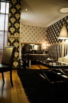 Una habitación con papel tapiz con estampado dorado y negro, un sillón de cuero negro, una mesa de centro de vidrio y una alfombra negra.