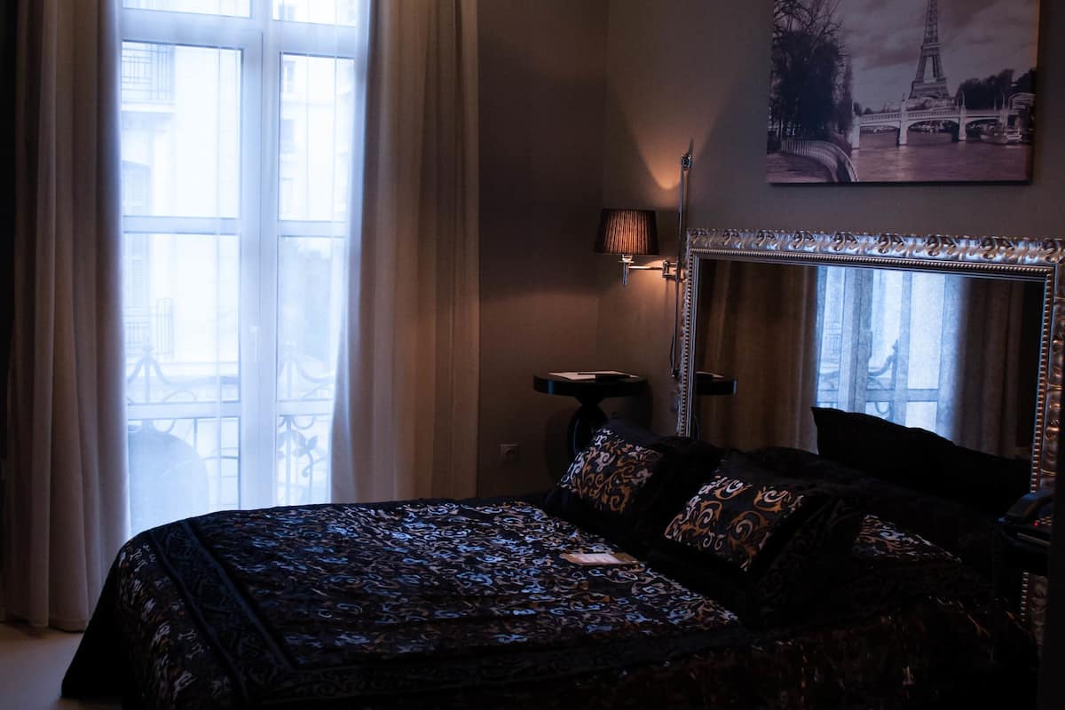 Un dormitori amb un llit gran, una làmpada penjant, una tauleta de nit, una làmpada, una finestra amb cortines i un quadre de la Torre Eiffel.