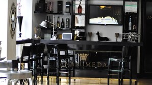 A bar area with a black counter, multiple chairs, a laptop, and various bottles and glasses. - Andromeda Hotel Thessaloniki (Thessaloniki)