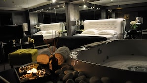 A modern hotel room with a large bathtub, two beds, a green ottoman, and a tray with candles and snacks. - Andromeda Hotel Thessaloniki (Thessaloniki)