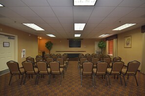 Un salón de conferencias con filas de sillas, un televisor de pantalla plana en la pared y piso alfombrado.