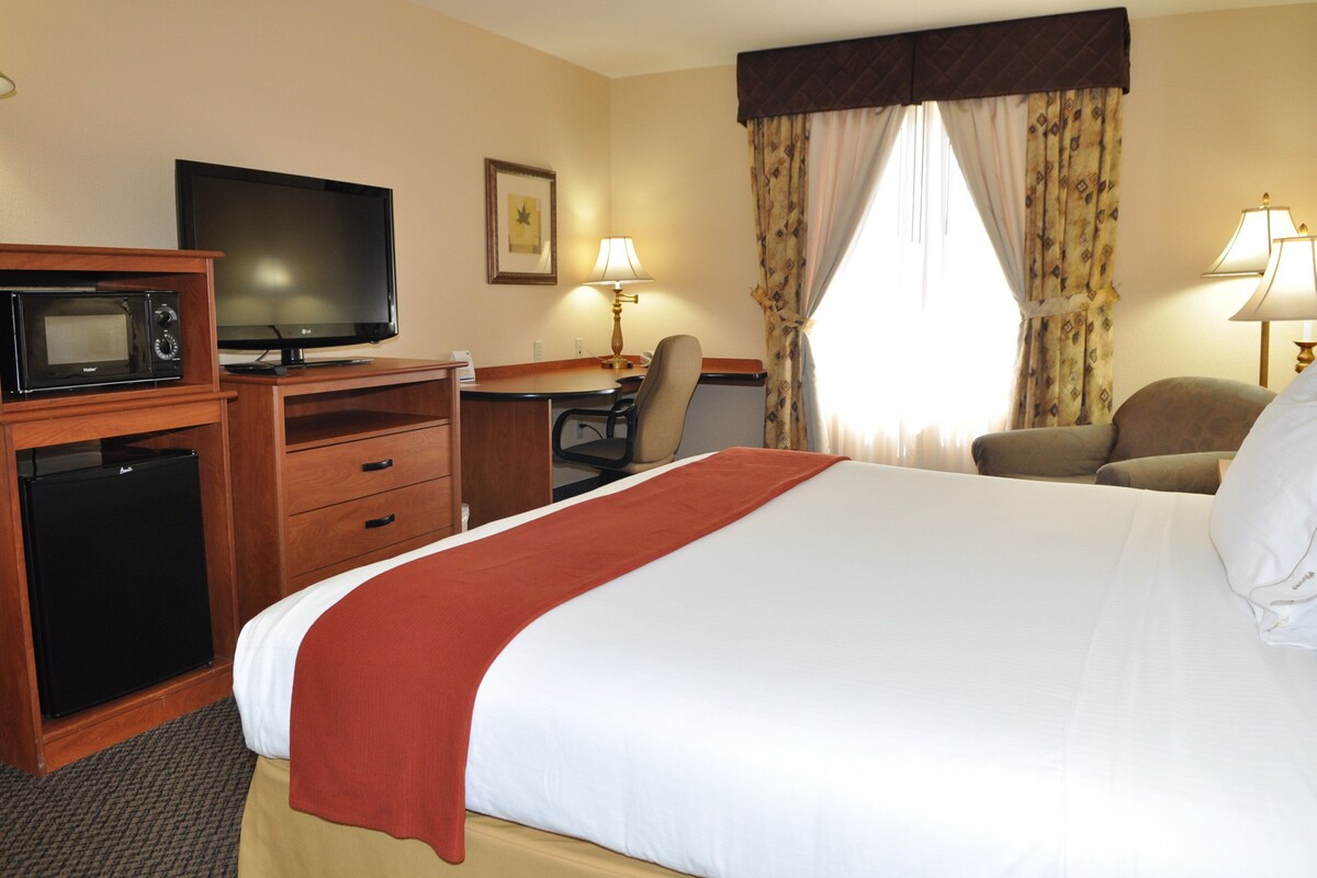 A hotel room with a bed, a desk with a computer, a television, a microwave, and a refrigerator.