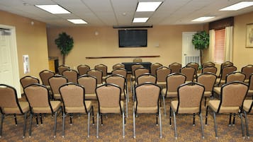 A conference room with rows of chairs, a flat-screen TV on the wall, and a potted plant.