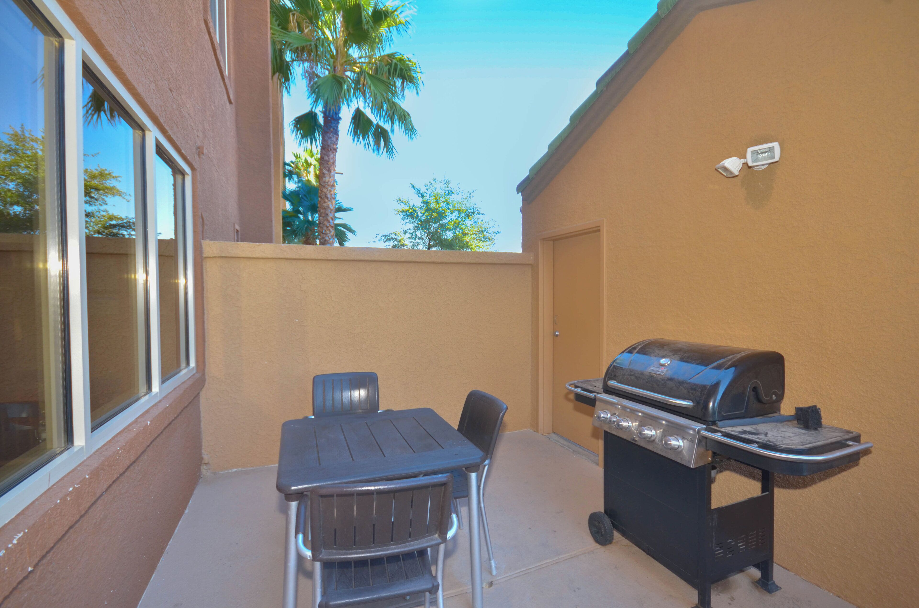 An outdoor patio with a grill, a table, and chairs.
