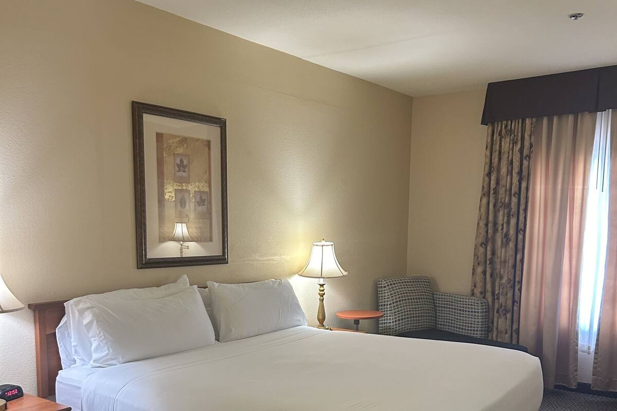 A hotel room with a large bed, a bedside table with a lamp, a small round table, and a framed picture on the wall.