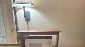 A compact kitchenette with a microwave and a small refrigerator, wooden cabinet, and a mirror above the microwave. - Holiday Inn Express Las Vegas-Nellis by IHG (Las Vegas)