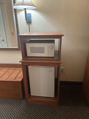 A compact kitchenette with a microwave and a small refrigerator, wooden cabinet, and a mirror above the microwave. - Holiday Inn Express Las Vegas-Nellis by IHG (Las Vegas)