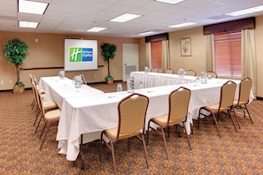 A conference room with a long table, chairs, a projector screen, and two potted plants. - Holiday Inn Express Las Vegas-Nellis by IHG (Las Vegas)