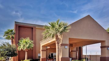 A hotel with a modern design, featuring a prominent entrance with a covered walkway and palm trees.