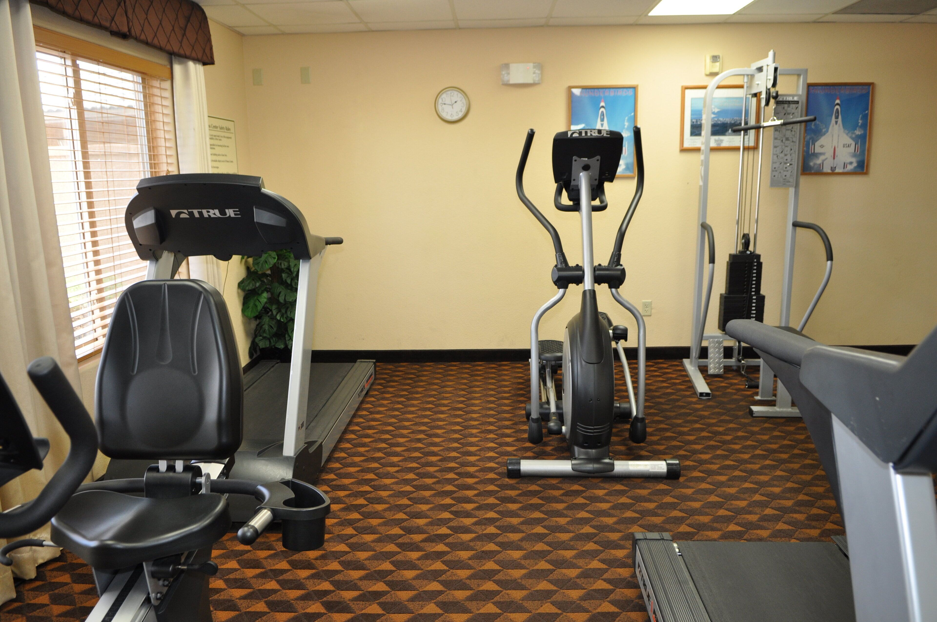 Ein Fitnessstudio mit Laufbändern, Hanteln und einer Wanduhr.