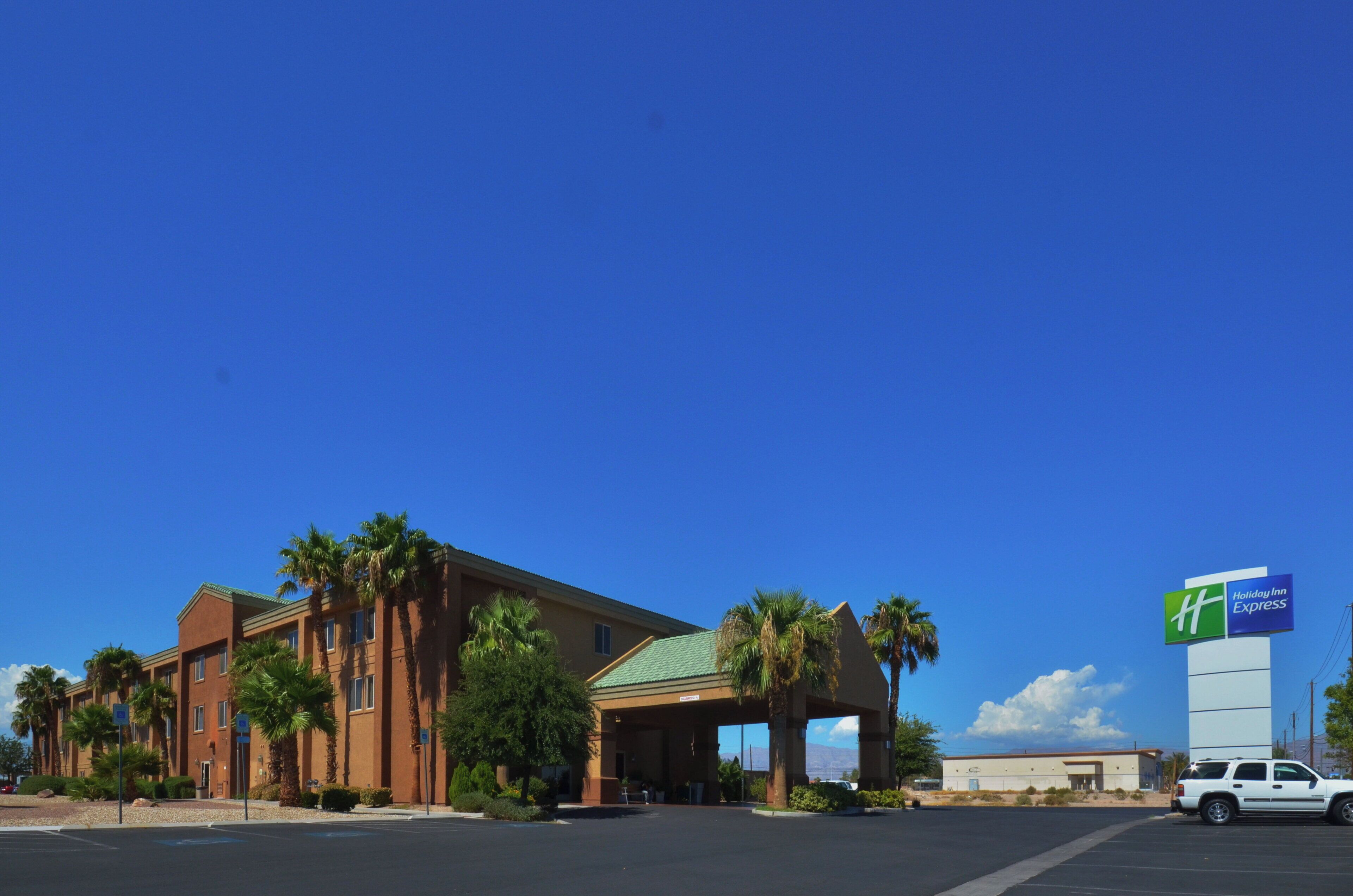 Un bâtiment de l’hôtel Holiday Inn Express avec un parking et des palmiers.