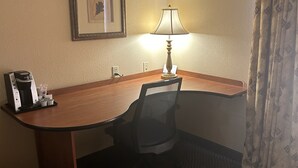 A hotel room with a wooden desk, a black office chair, a lamp, a framed picture on the wall, a coffee maker, and a trash bin. - Holiday Inn Express Las Vegas-Nellis by IHG (Las Vegas)