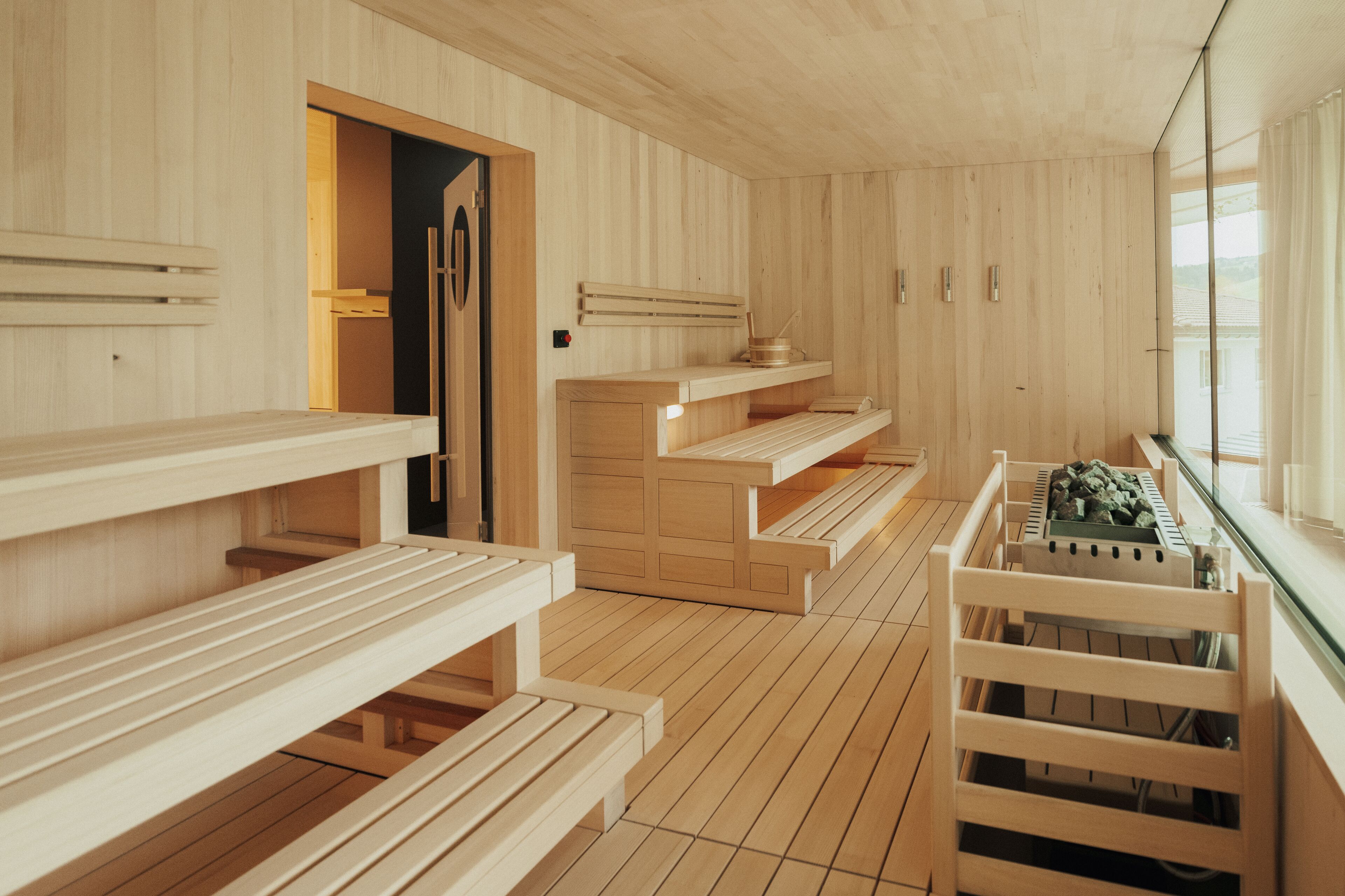 A wooden sauna with benches and a bench with a basket of stones.