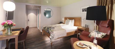Une chambre d’hôtel avec un lit, un bureau, une chaise, une table et une lampe.