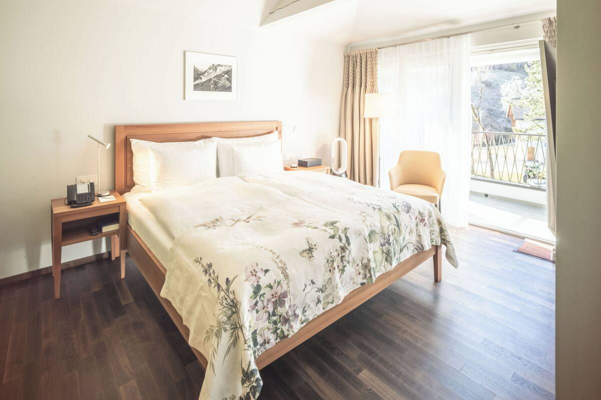 Une chambre à coucher comprenant un lit, une table de chevet, une lampe, une chaise et une fenêtre avec des rideaux.