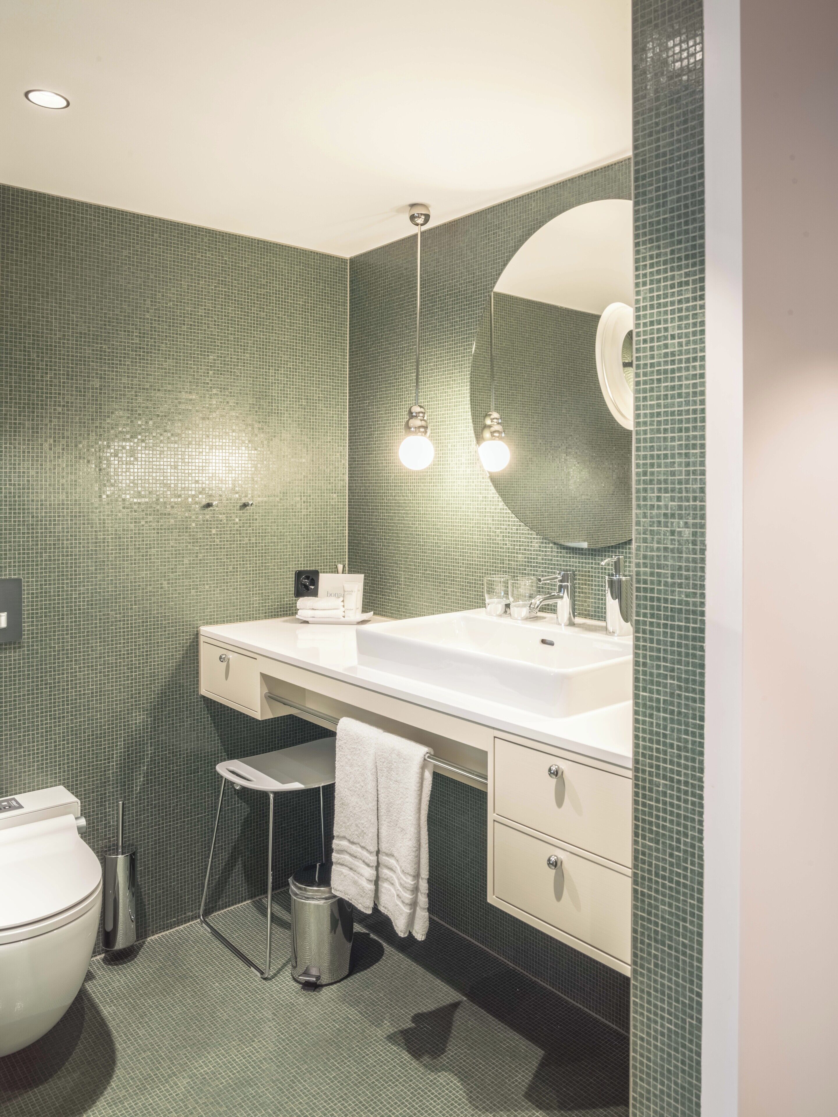 Une salle de bain moderne avec un grand miroir, deux lavabos, des toilettes et un petit tabouret.