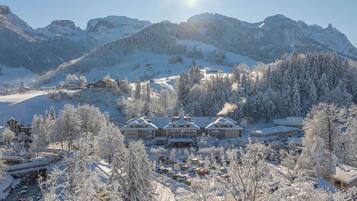 A snow-covered mountain resort with multiple buildings, a bridge, and a parking area.
