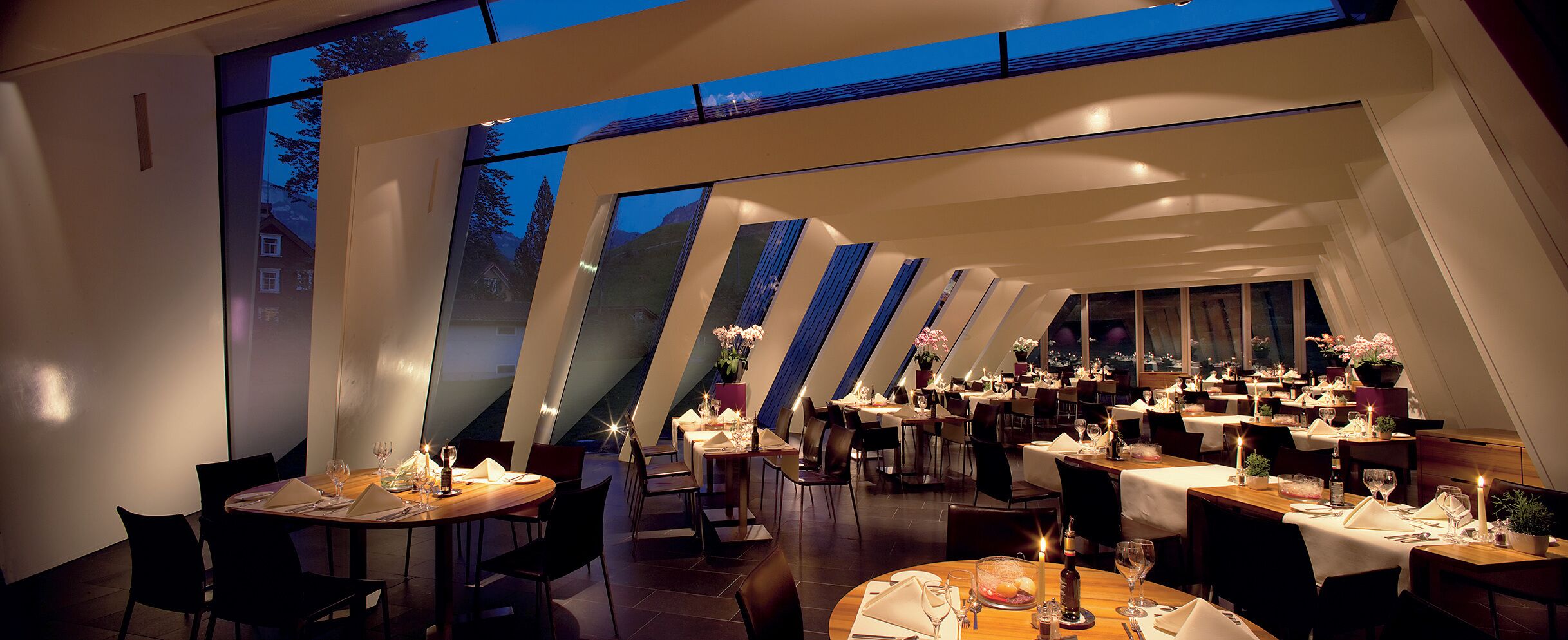 Un restaurante moderno con varias mesas de comedor, cada una decorada con velas y flores.