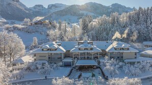Un hotel grande y moderno con varias construcciones, rodeado de árboles nevados y montañas.