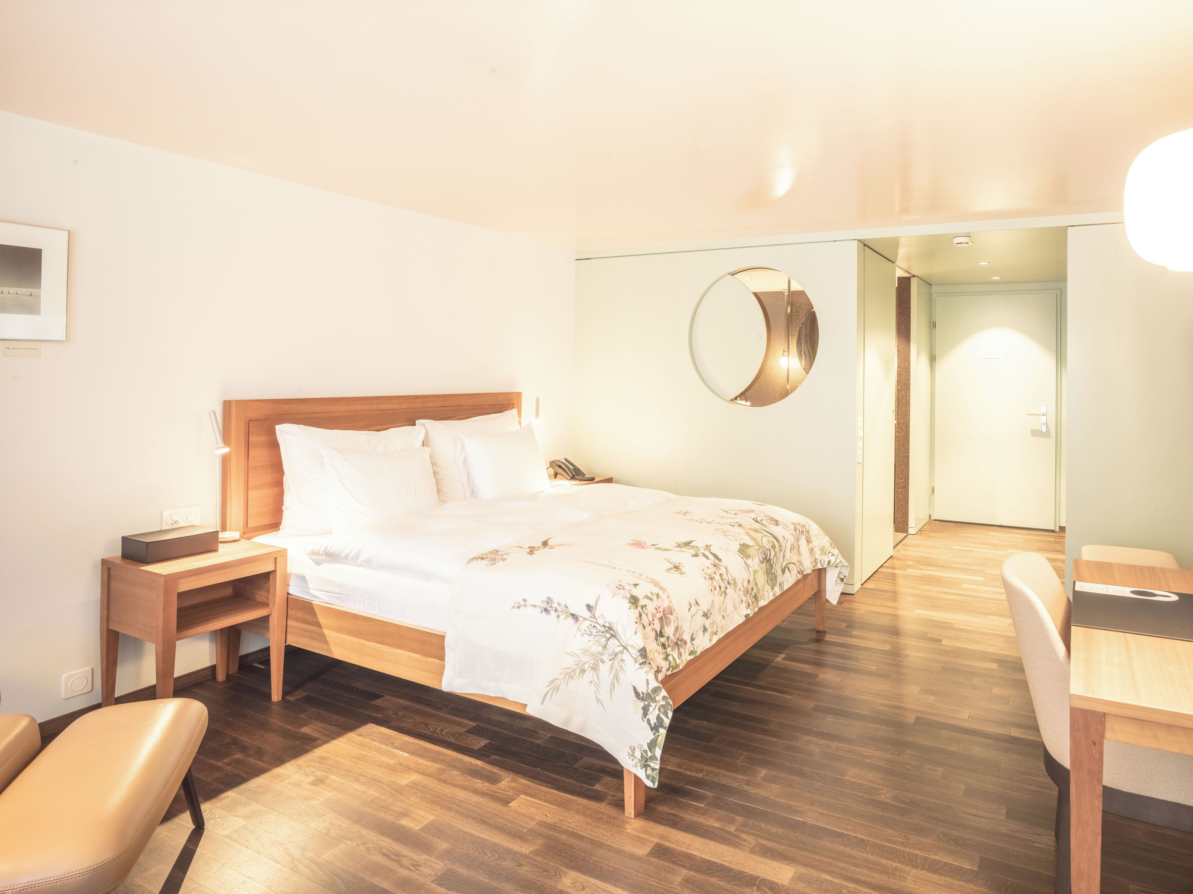 Ein Hotelzimmer mit einem hölzernen Bett, einem Nachttisch, einem Sessel und einem Schreibtisch.