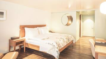Ein Hotelzimmer mit einem hölzernen Bett, einem Nachttisch, einem Sessel und einem Schreibtisch.