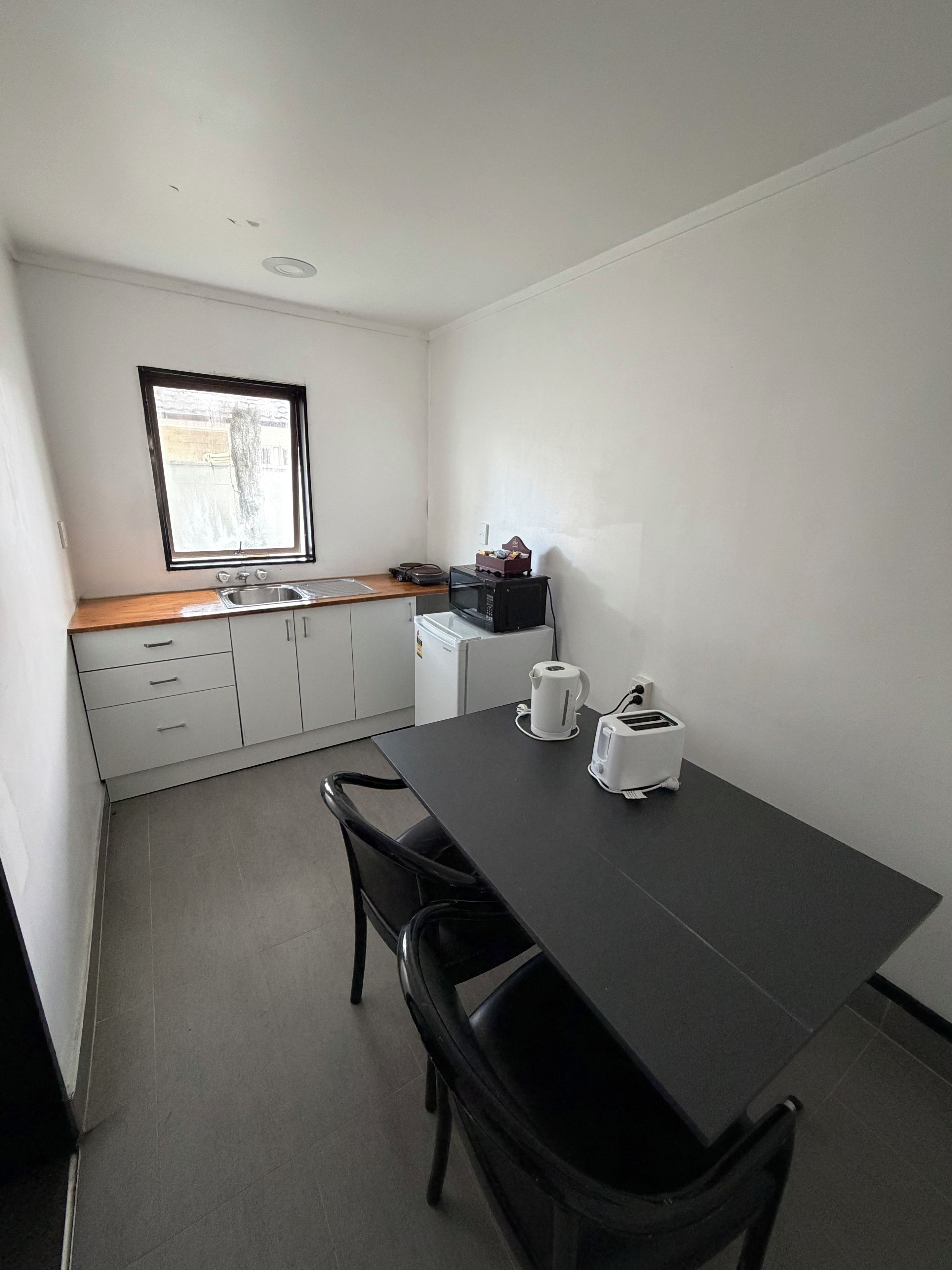A compact kitchen with a dining table, two chairs, a microwave, a kettle, and a toaster.