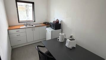 A compact kitchen with a dining table, two chairs, a microwave, a kettle, and a toaster.
