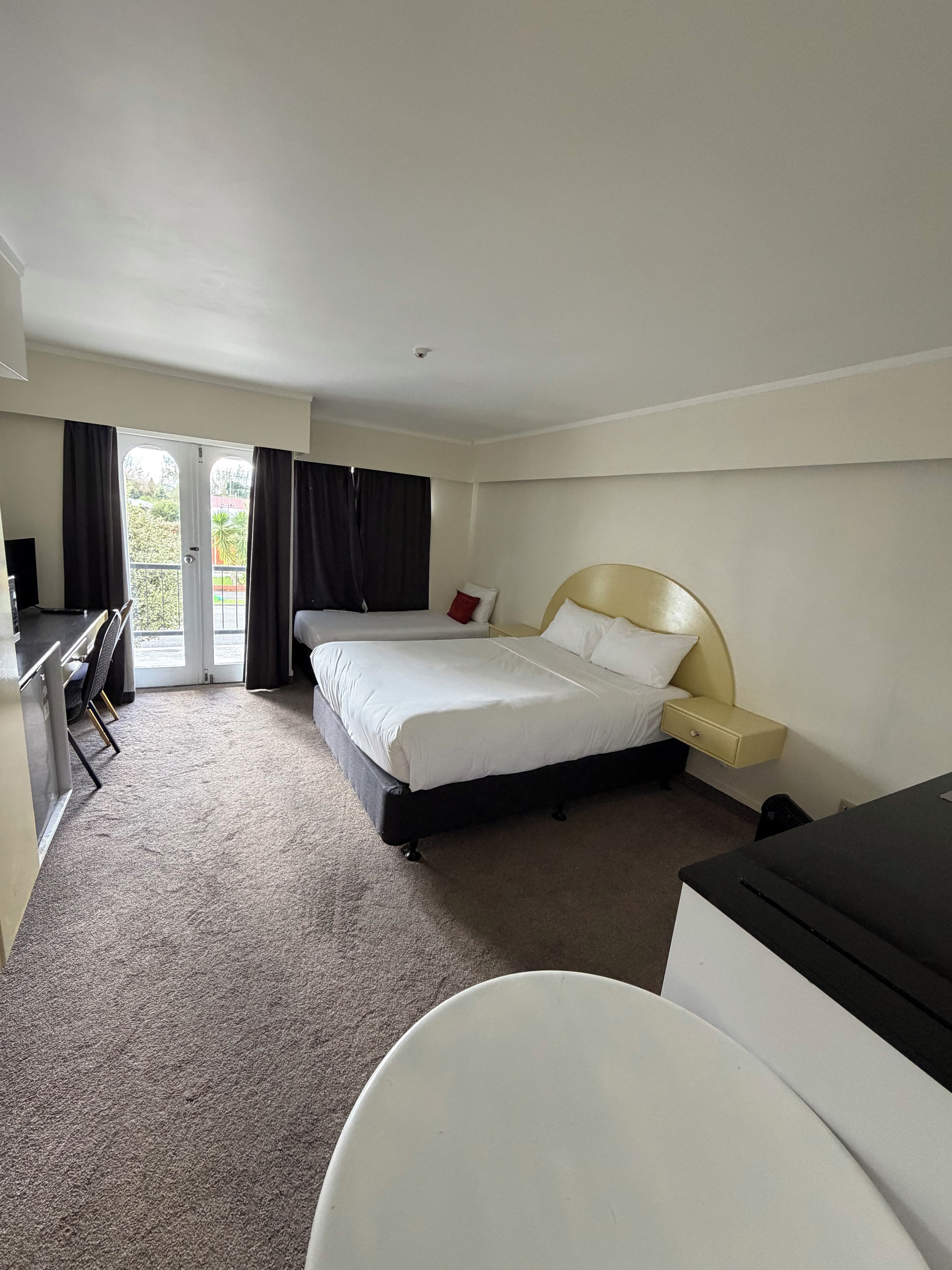 A hotel room with a bed, bedside table, desk, and a view through a door.