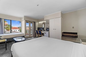 Habitación de hotel con una cama grande, un escritorio con silla, una kitchenette pequeña y vistas al exterior.