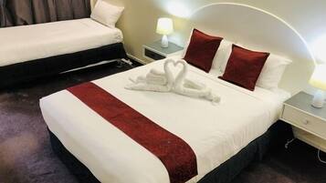 Een hotelkamer met een groot bed, een kleiner bed en een nachtkastje met een lamp.