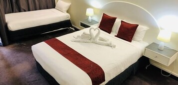 Una habitación de hotel con una cama grande, una cama más pequeña y una mesita de noche con una lámpara.