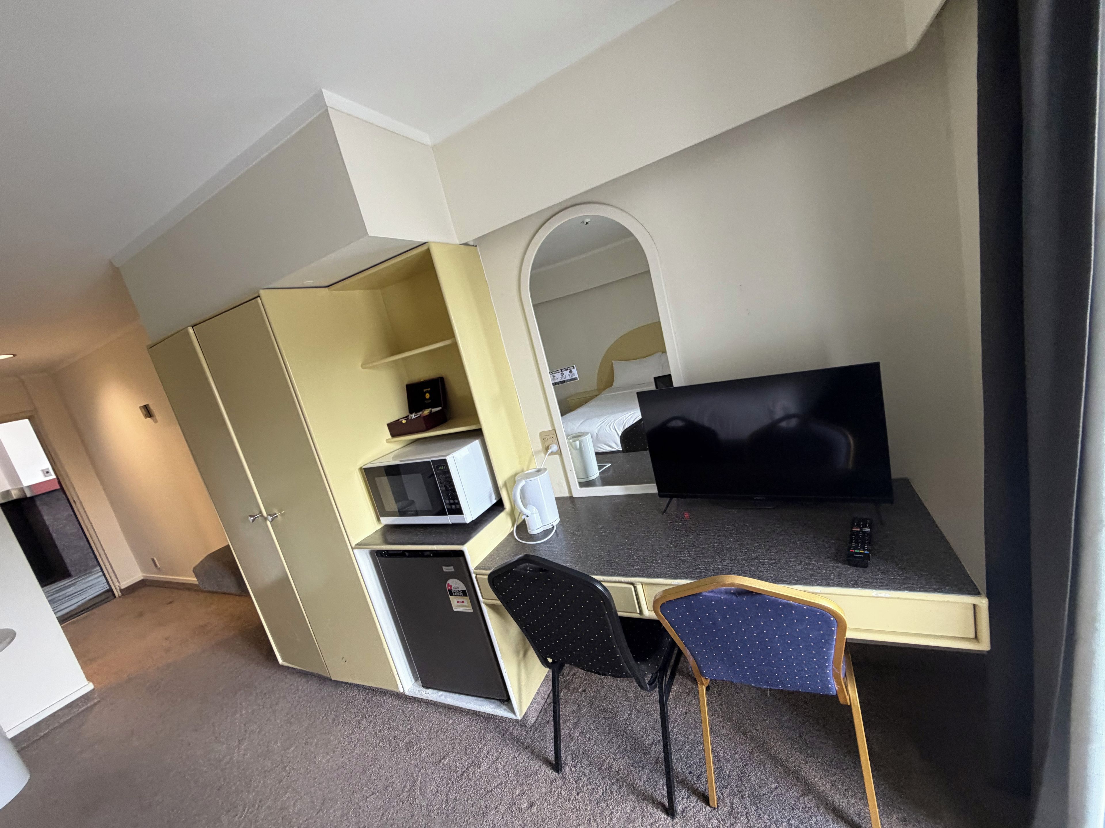 Una habitación compacta con kitchenette, una cama, un televisor y un escritorio con silla.