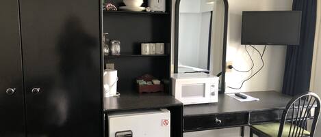 Habitación de hotel compacta con kitchenette, pequeño refrigerador, microondas, televisión de pantalla plana, una silla y un espejo.
